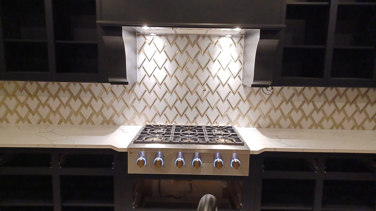 Gold lattice tile backsplash behind a six-burner gas cooktop and range hood