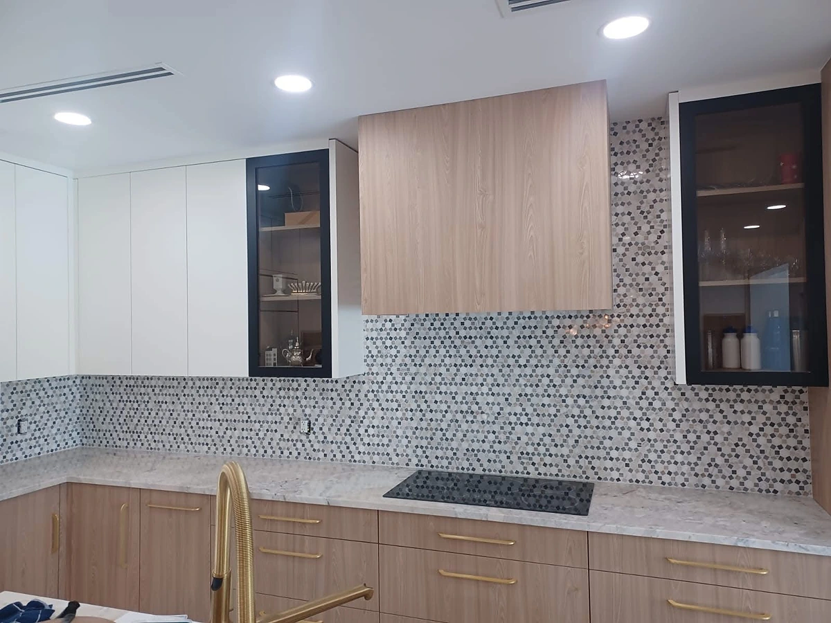 Gray mosaic tile backsplash paired with wood cabinetry and a brass faucet