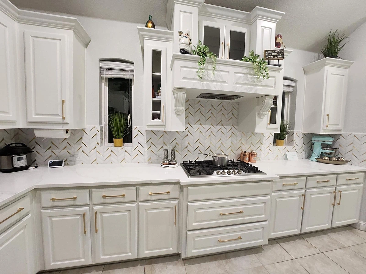 White herringbone marble backsplash behind a range with gold hardware