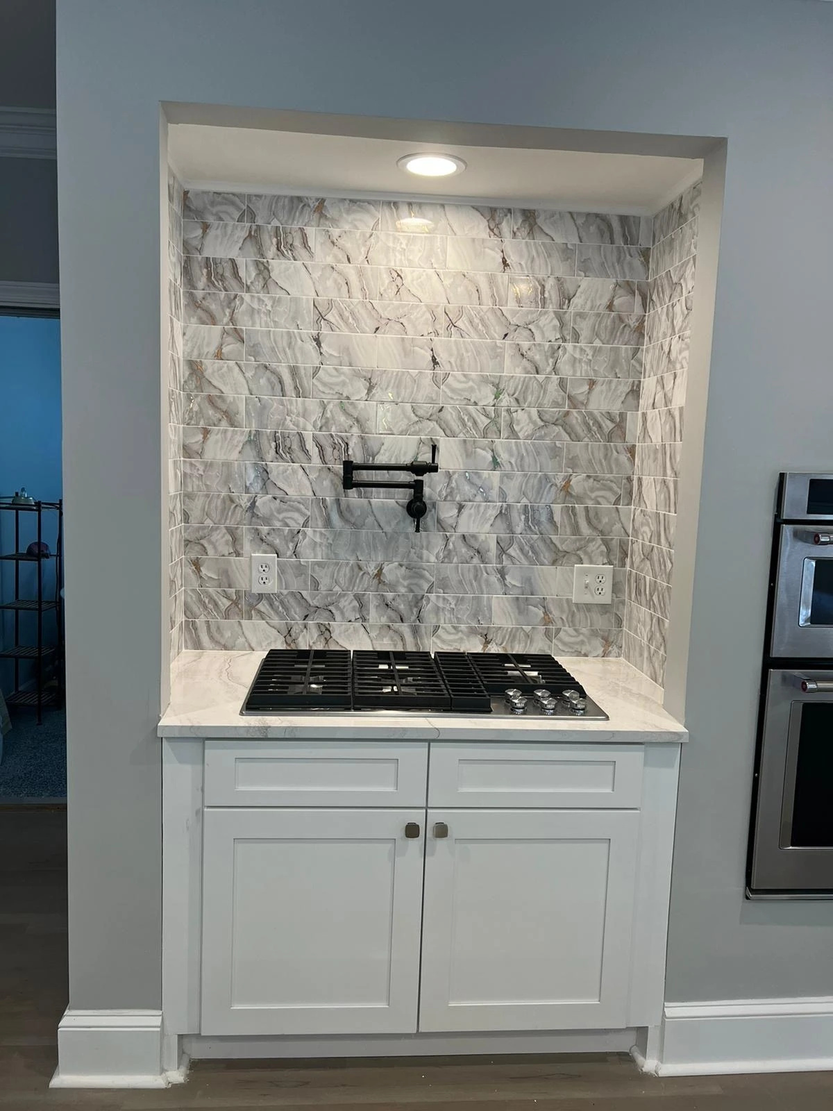 Stacked stone tile backsplash behind a gas cooktop with a pot filler and white cabinetry