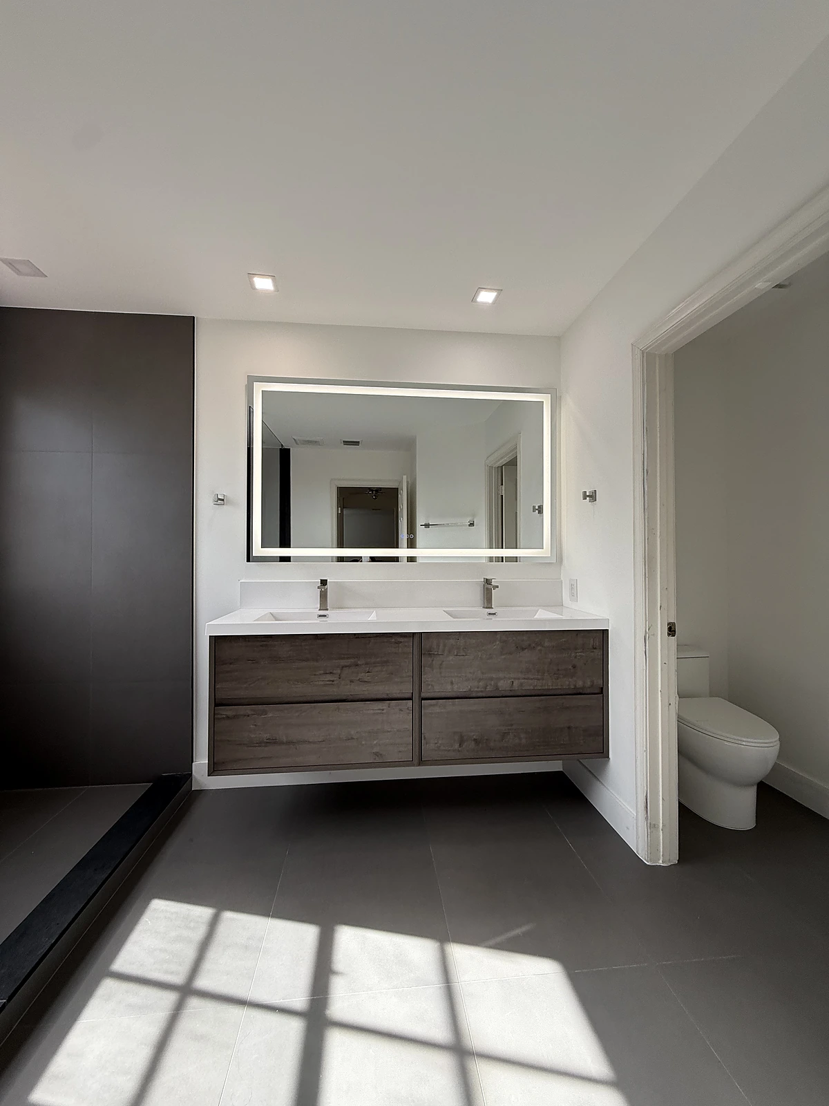 Double wood vanity with LED mirror over dark porcelain flooring