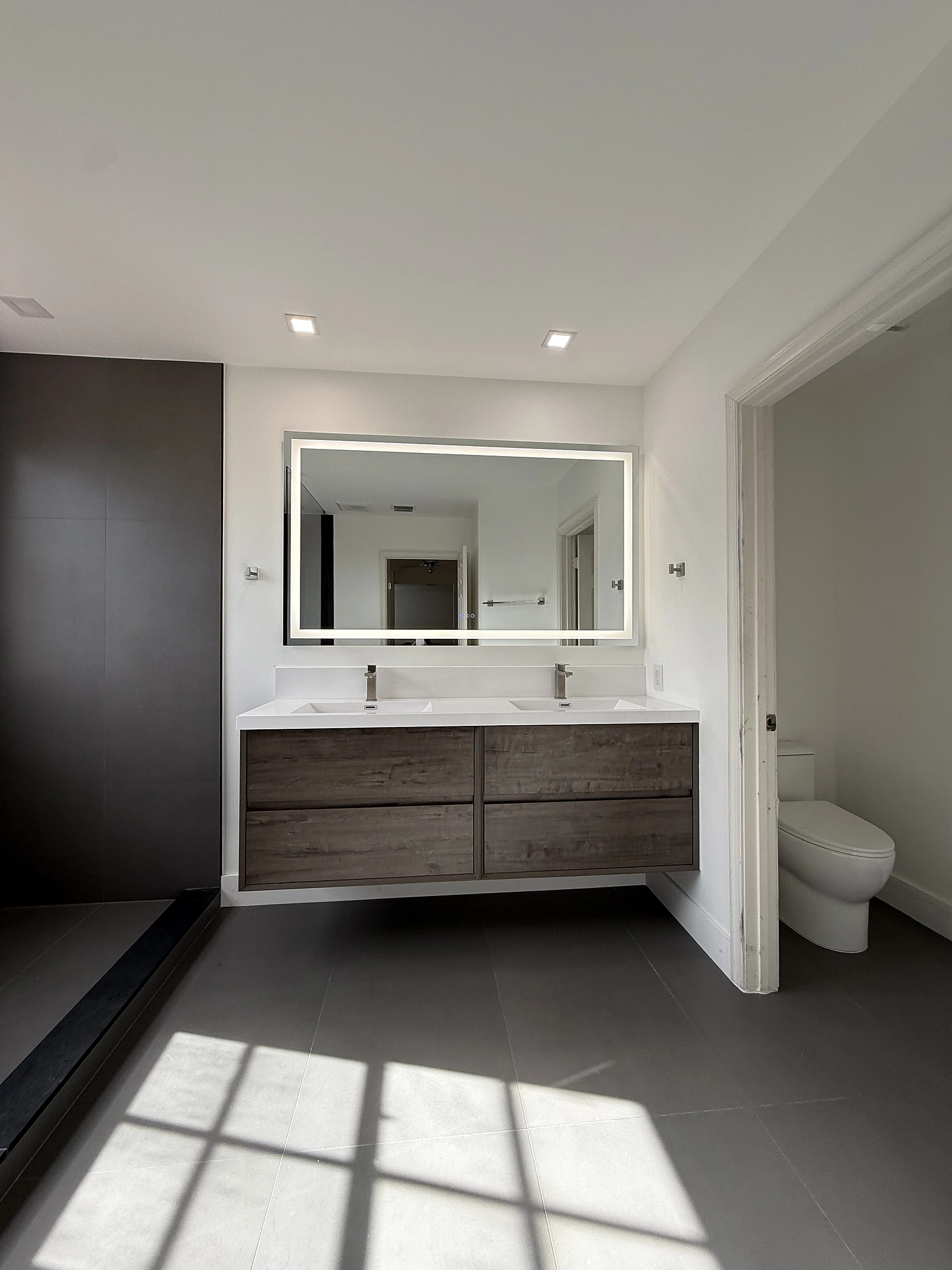 Double wood vanity with LED mirror over dark porcelain flooring — West Palm Beach, FL