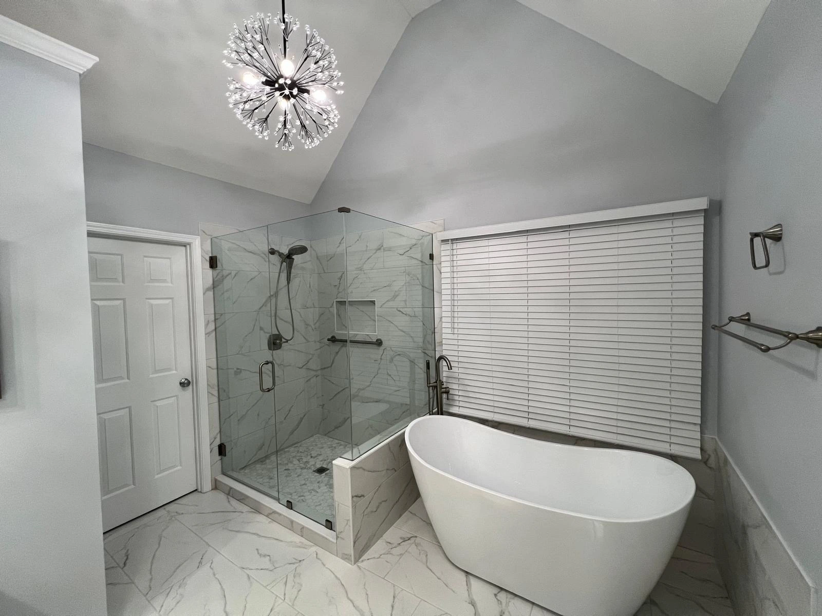 Freestanding soaking tub beside a marble walk-in shower under a modern chandelier — Deerfield Beach, FL