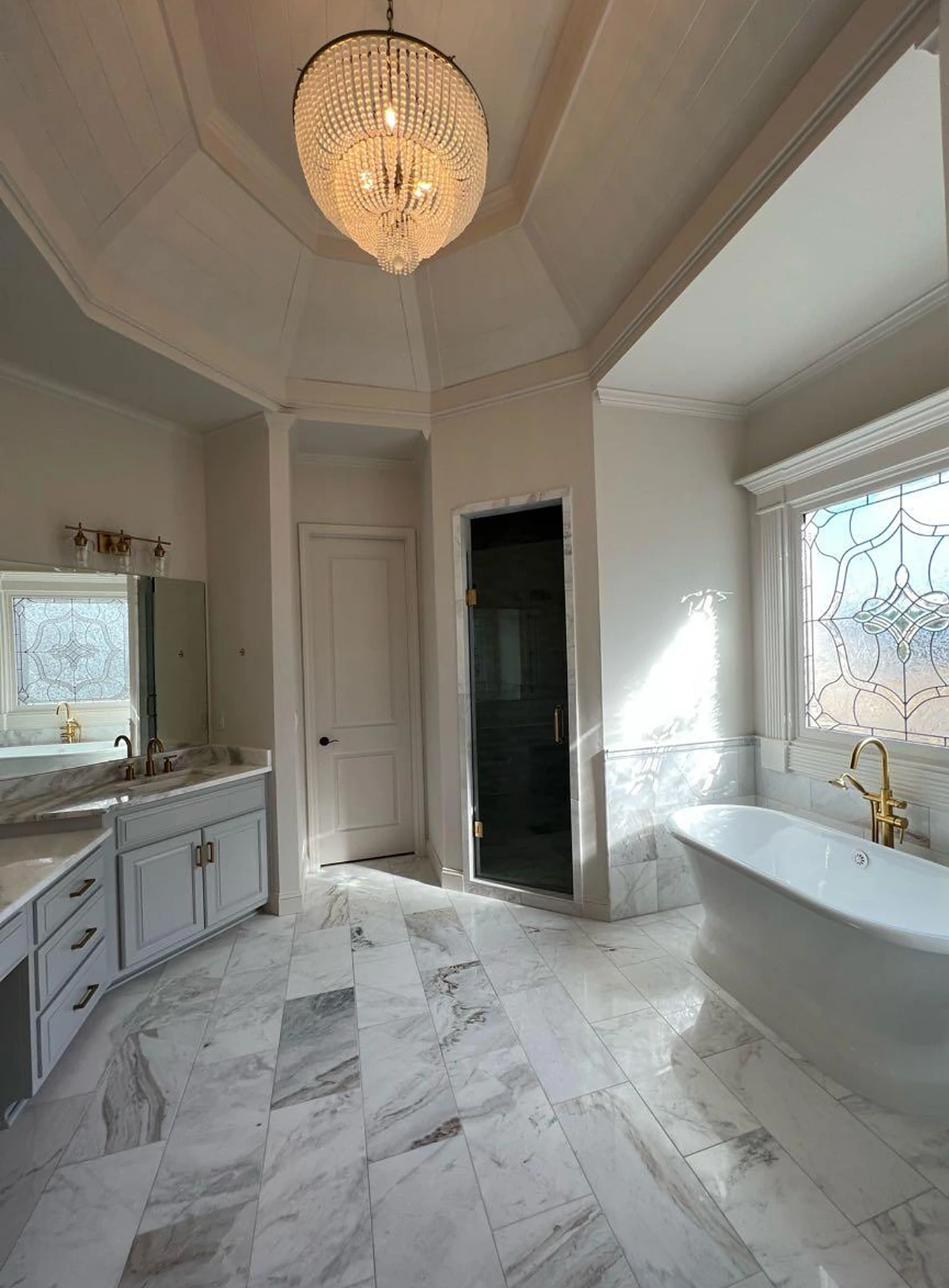 Freestanding tub on marble flooring beneath a chandelier