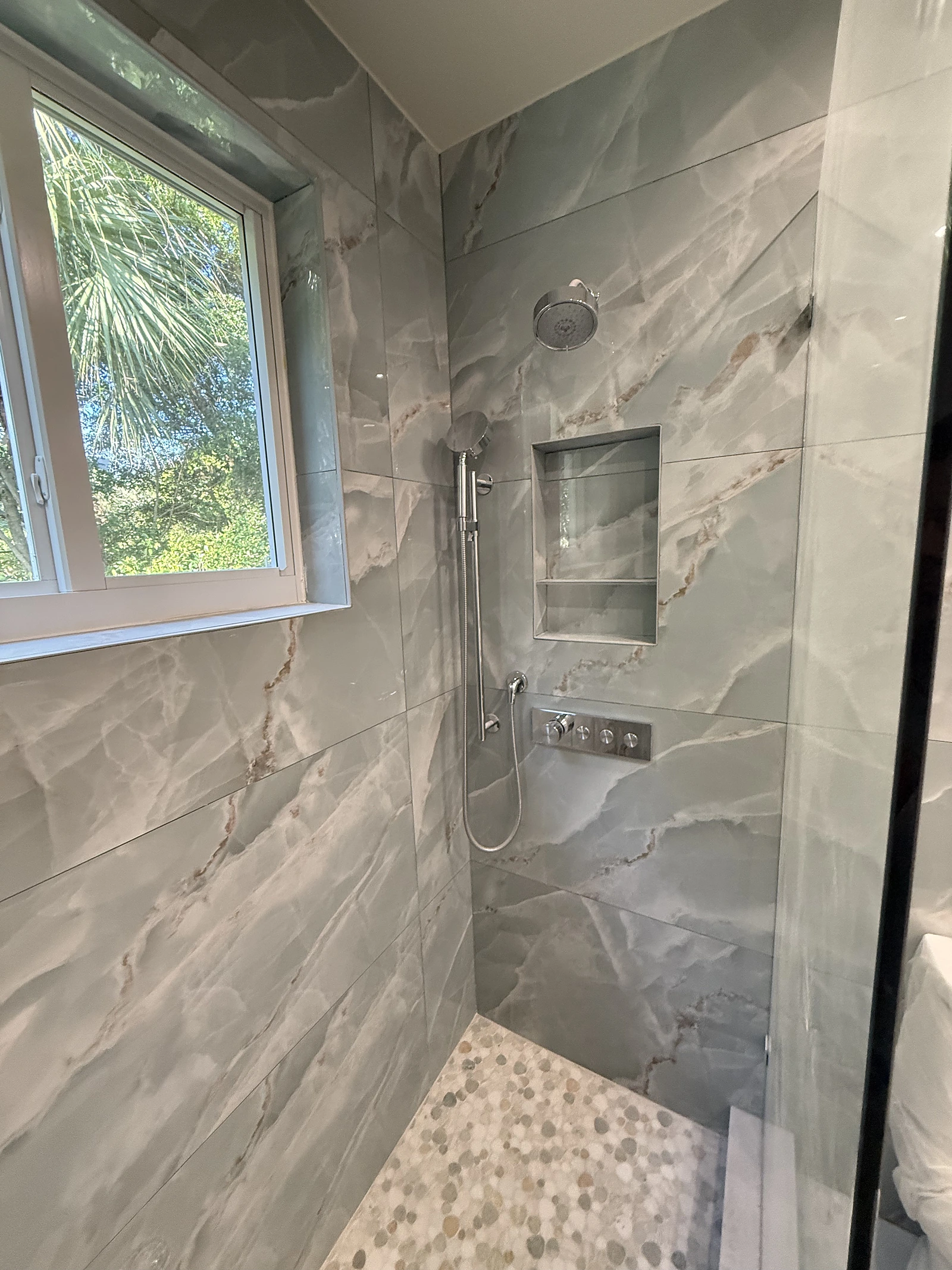 Grey stone-look tile shower with window and pebble accent floor — Miami, FL