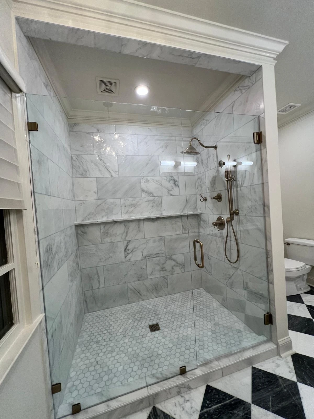 Walk-in shower with marble tile surround and black-and-white checkered floor in a South Florida bathroom remodel — Pompano Beach, FL