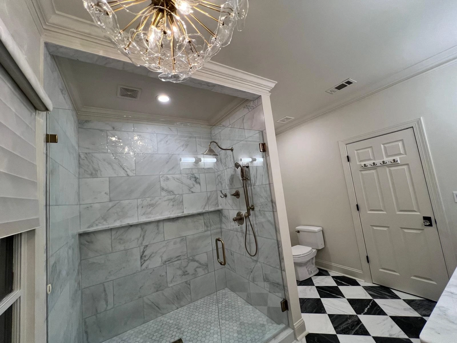 Marble shower enclosure lit by a crystal chandelier in a South Florida master bathroom — Hollywood, FL