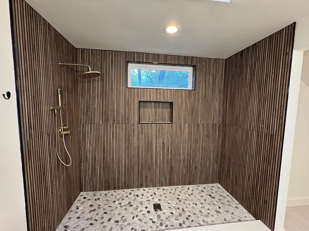 Walk-in shower with vertical wood-look ribbed tile and pebble stone floor by Primer Star Corp