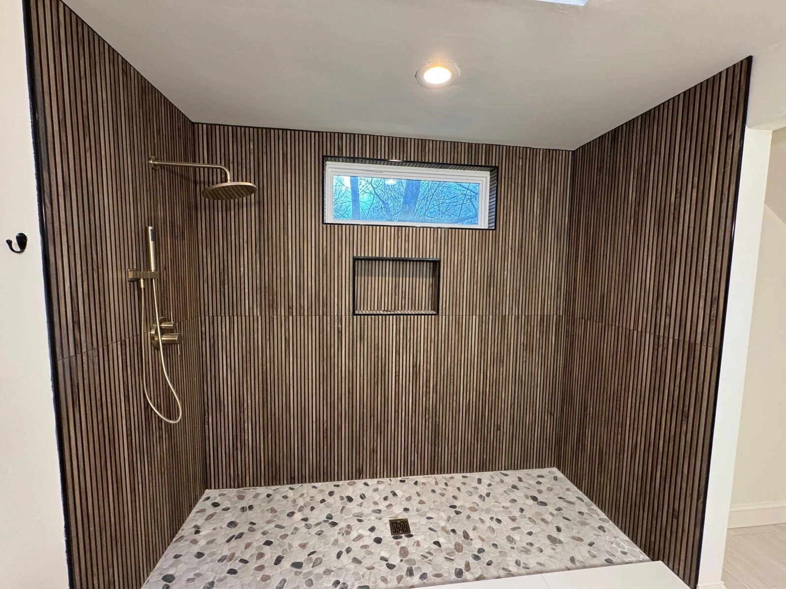 Walk-in shower with vertical wood-look ribbed tile and pebble stone floor by Primer Star Corp — Pompano Beach, FL