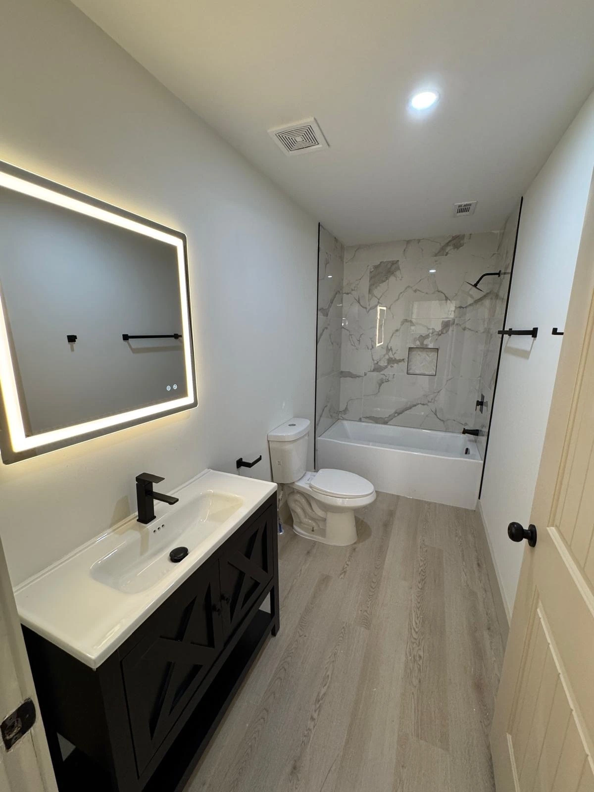 Compact bathroom remodel with marble tub-shower surround and black vanity — Hollywood, FL