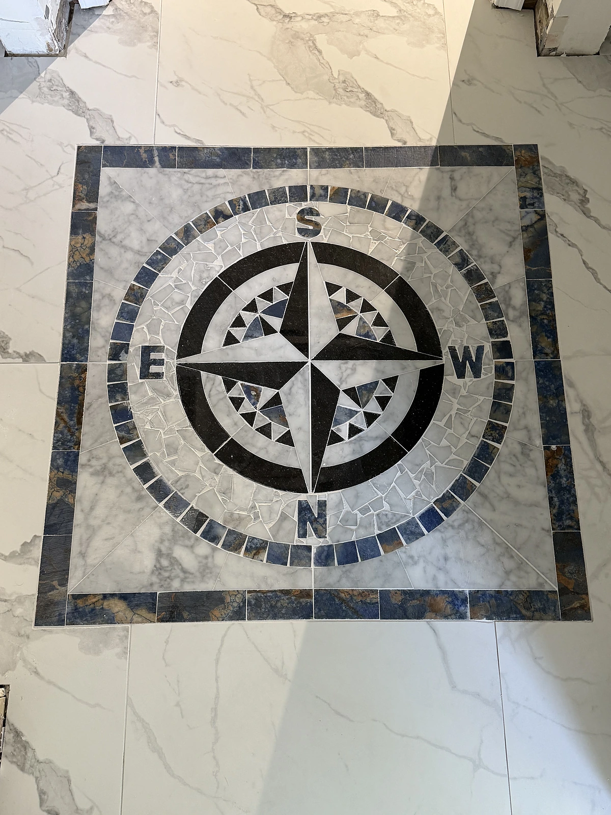 Compass rose mosaic medallion inlaid in a marble-look tile floor