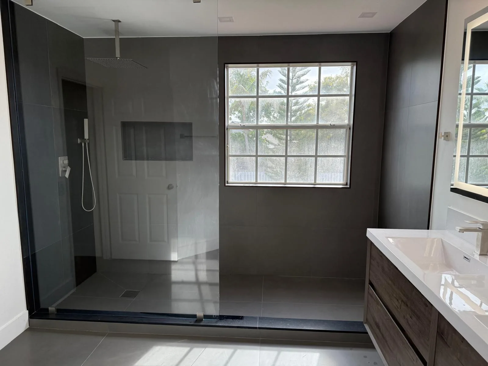 Dark tile walk-in shower with window and wood vanity — Fort Lauderdale, FL