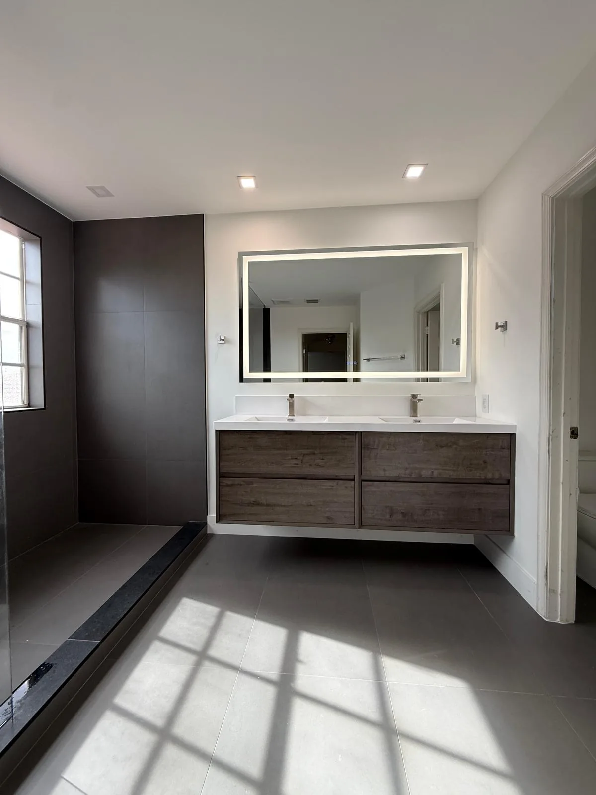 Floating wood vanity with backlit mirror in a sunlit bathroom — Fort Lauderdale, FL