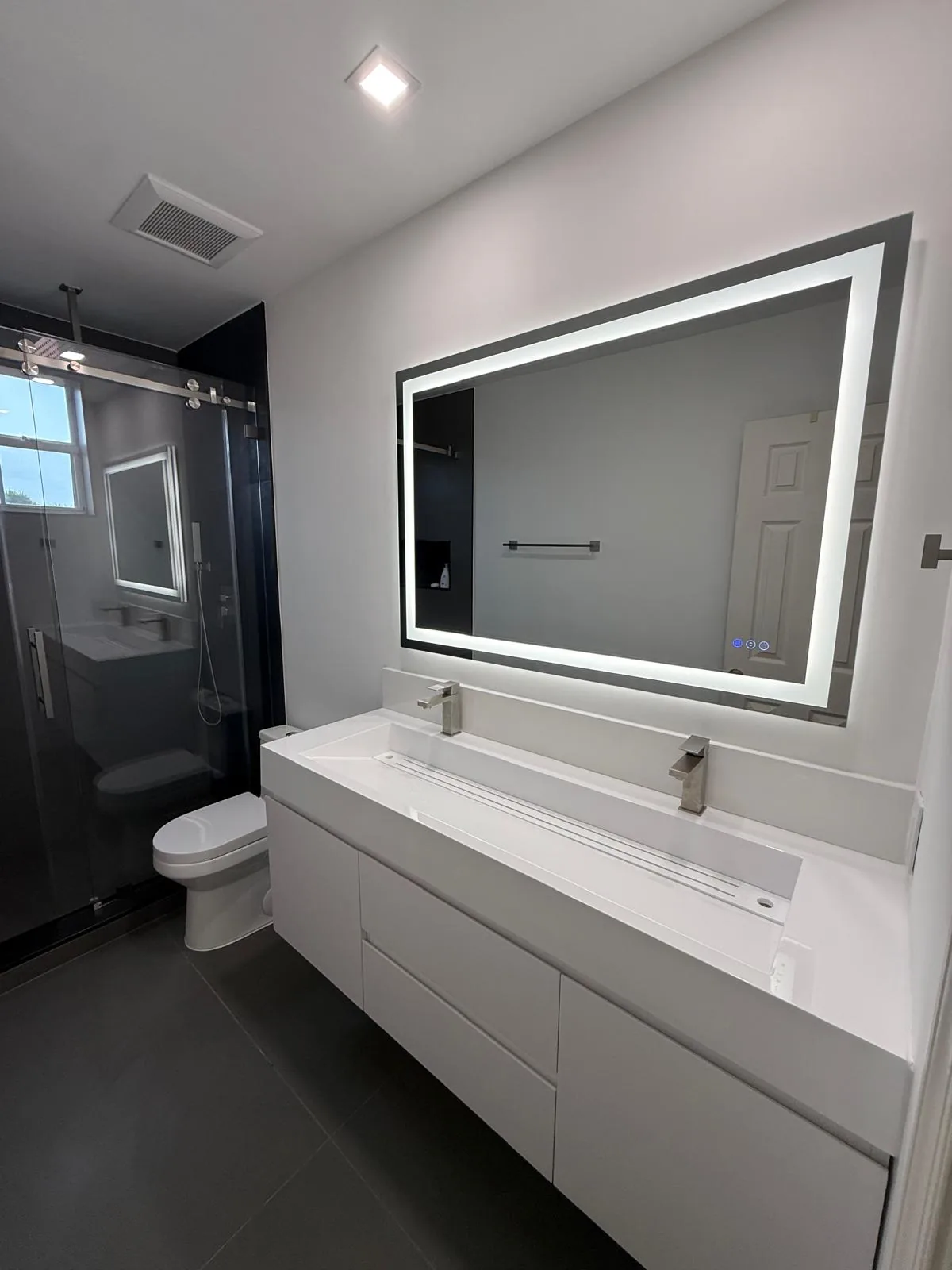 Compact bathroom with backlit mirror, white vanity and dark shower — Fort Lauderdale, FL