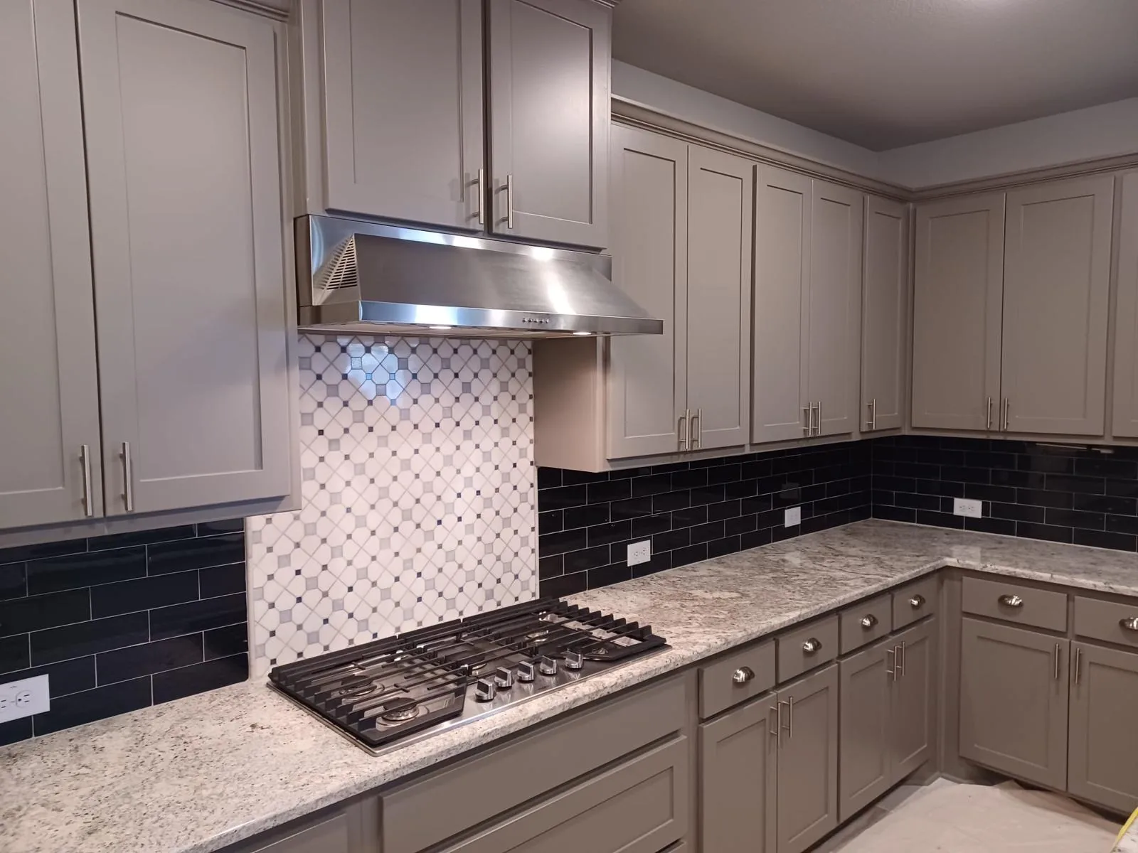 Kitchen cooktop wall with tile backsplash and stainless range hood