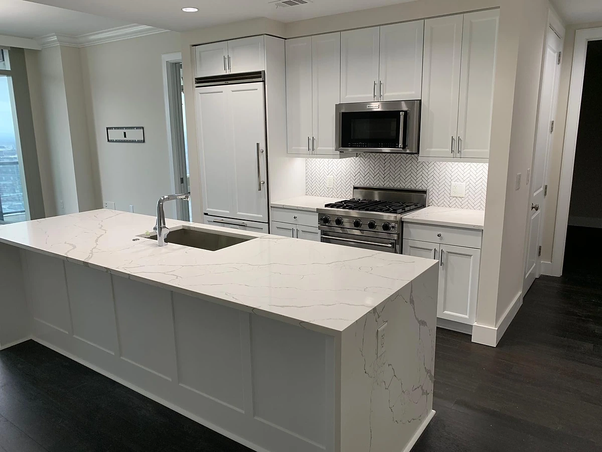 White kitchen with a Calacatta quartz waterfall island, stainless range and mosaic backsplash