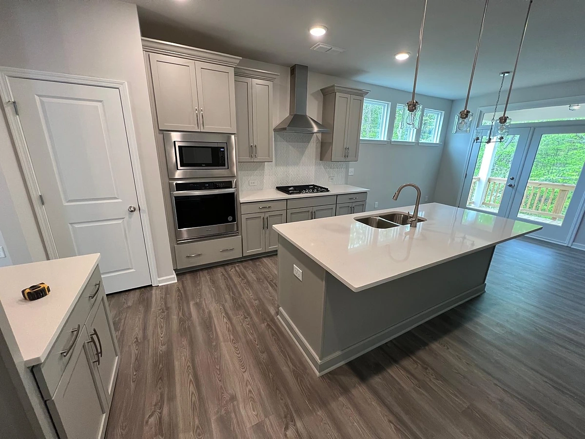 White kitchen with a gray waterfall island, built-in wall oven and wood-look flooring