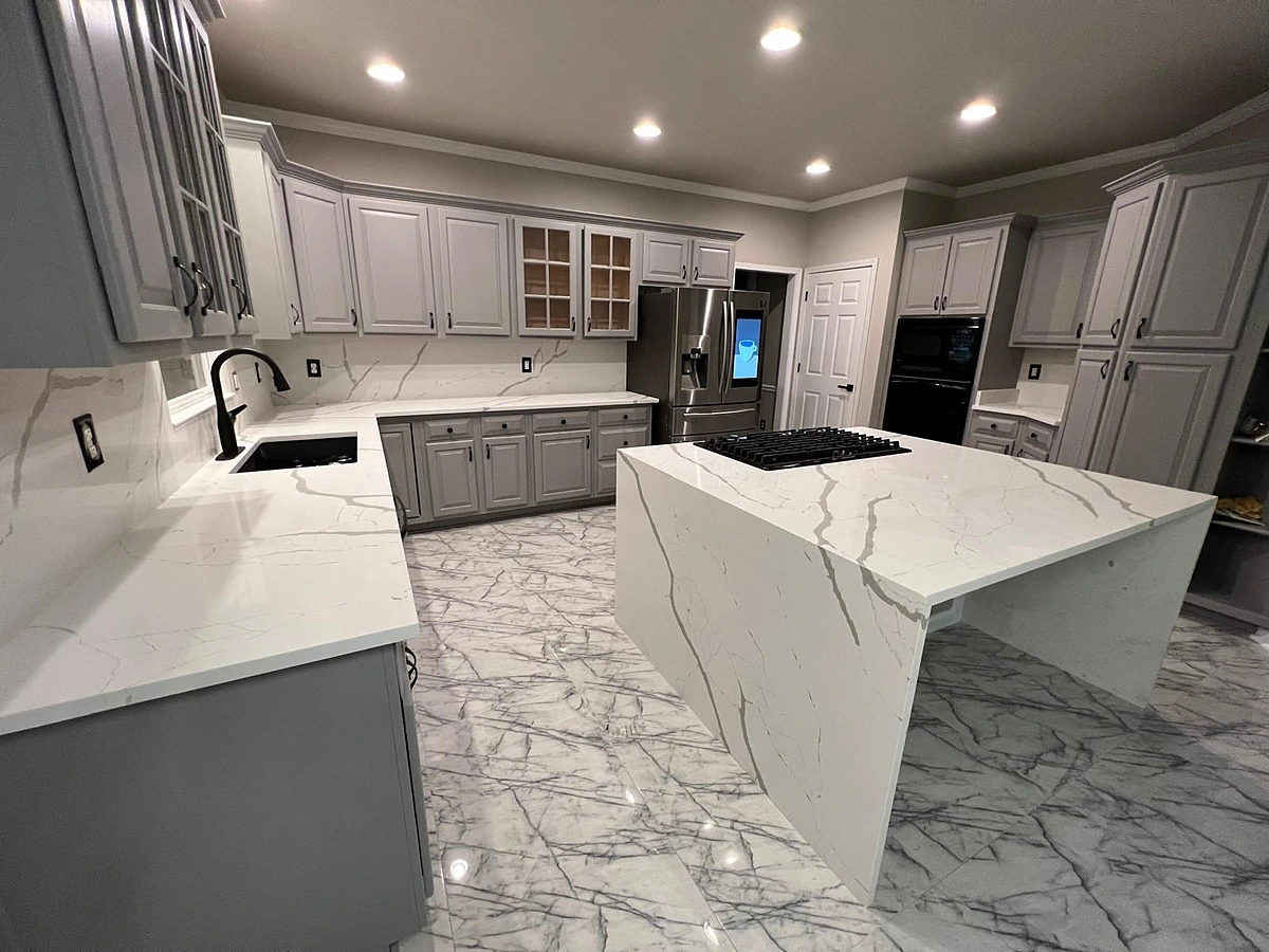 Gray and white kitchen with a marble waterfall island and glass display cabinets