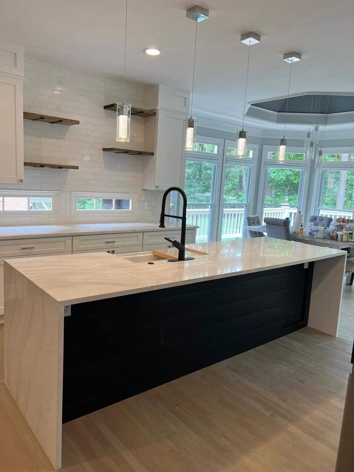 White kitchen with a navy island, floating oak shelves and black fixtures beside garden windows