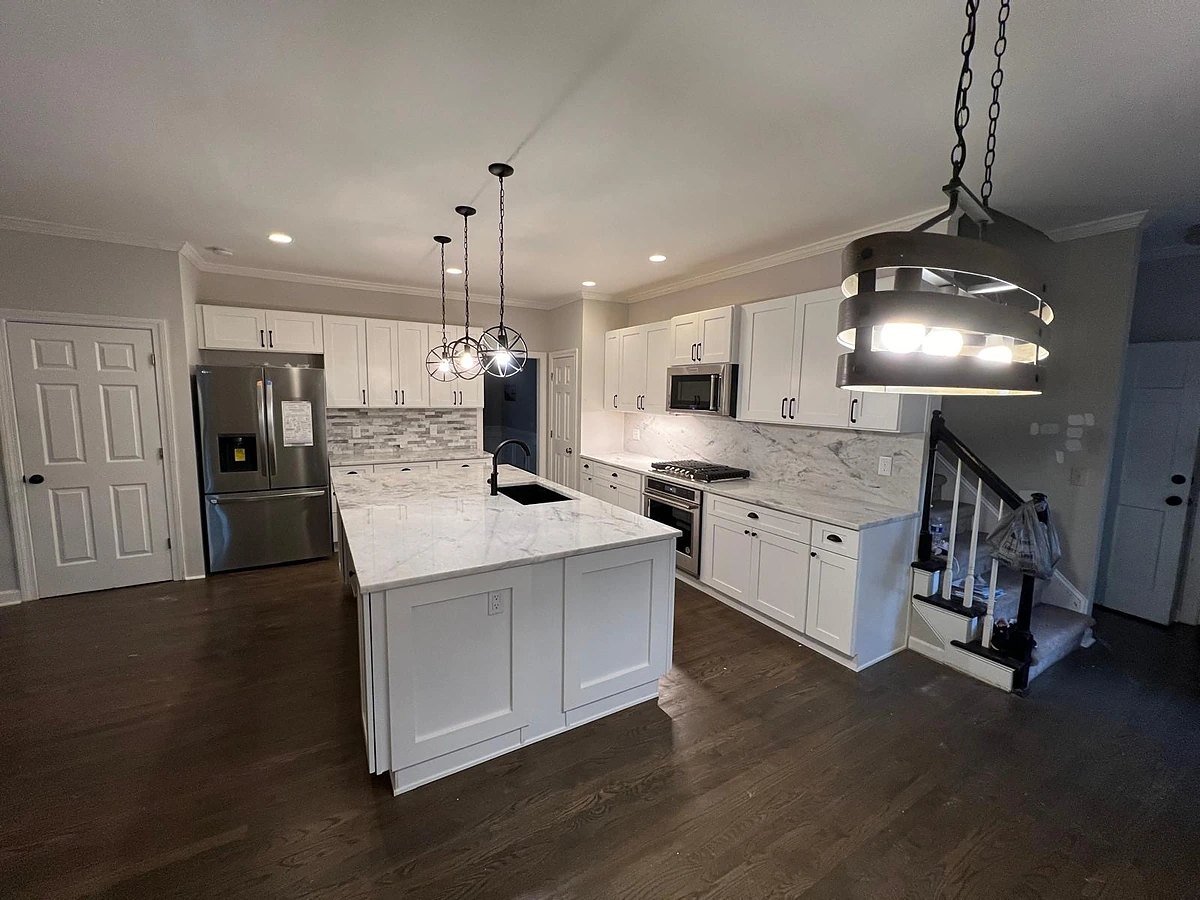 Open-plan white kitchen with a marble waterfall island and glass globe pendants