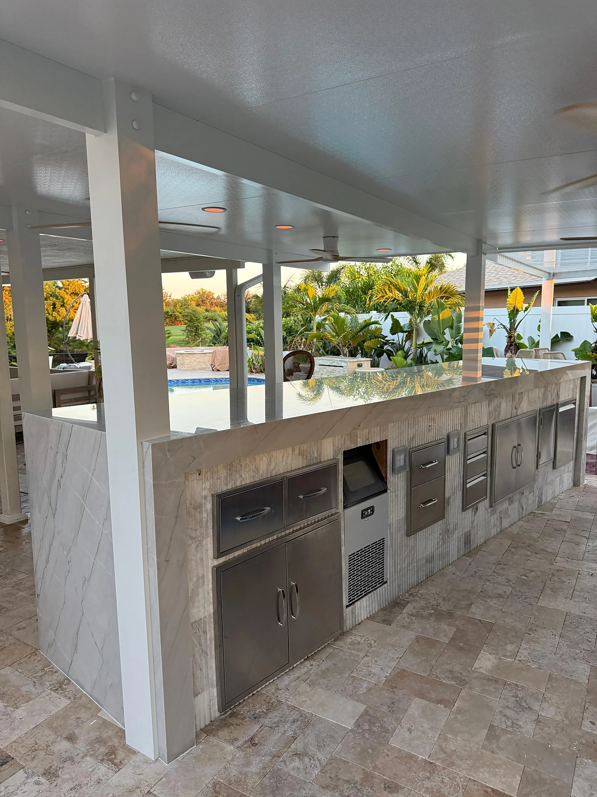 Poolside outdoor kitchen with stainless appliances and a marble waterfall countertop