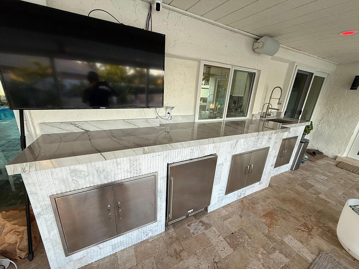 Outdoor kitchen run with stainless appliances and a marble countertop beside sliding glass doors