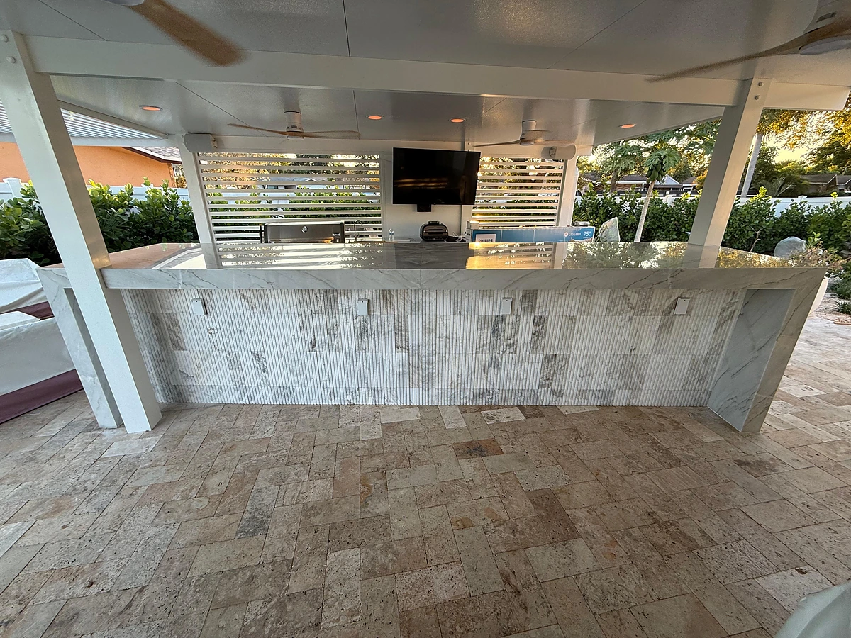 Covered outdoor kitchen with a stacked-stone bar, stone countertop and travertine patio floor