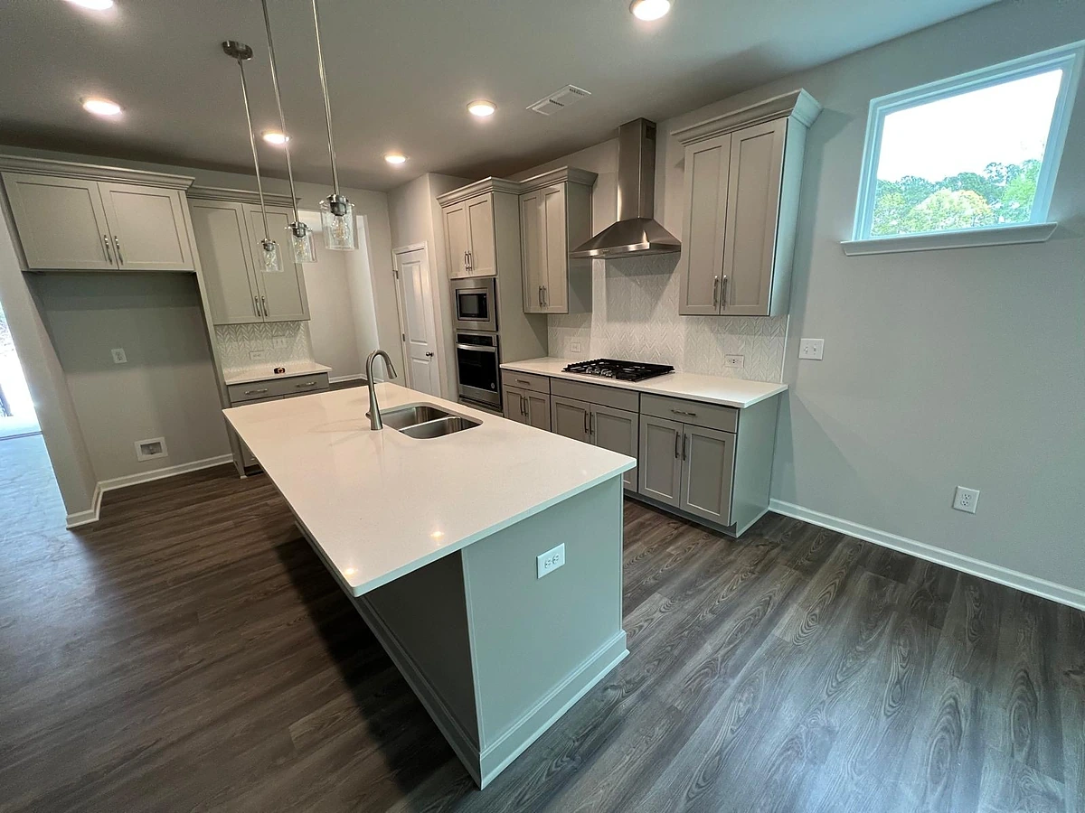 Sage-gray kitchen with a white waterfall island and double wall ovens