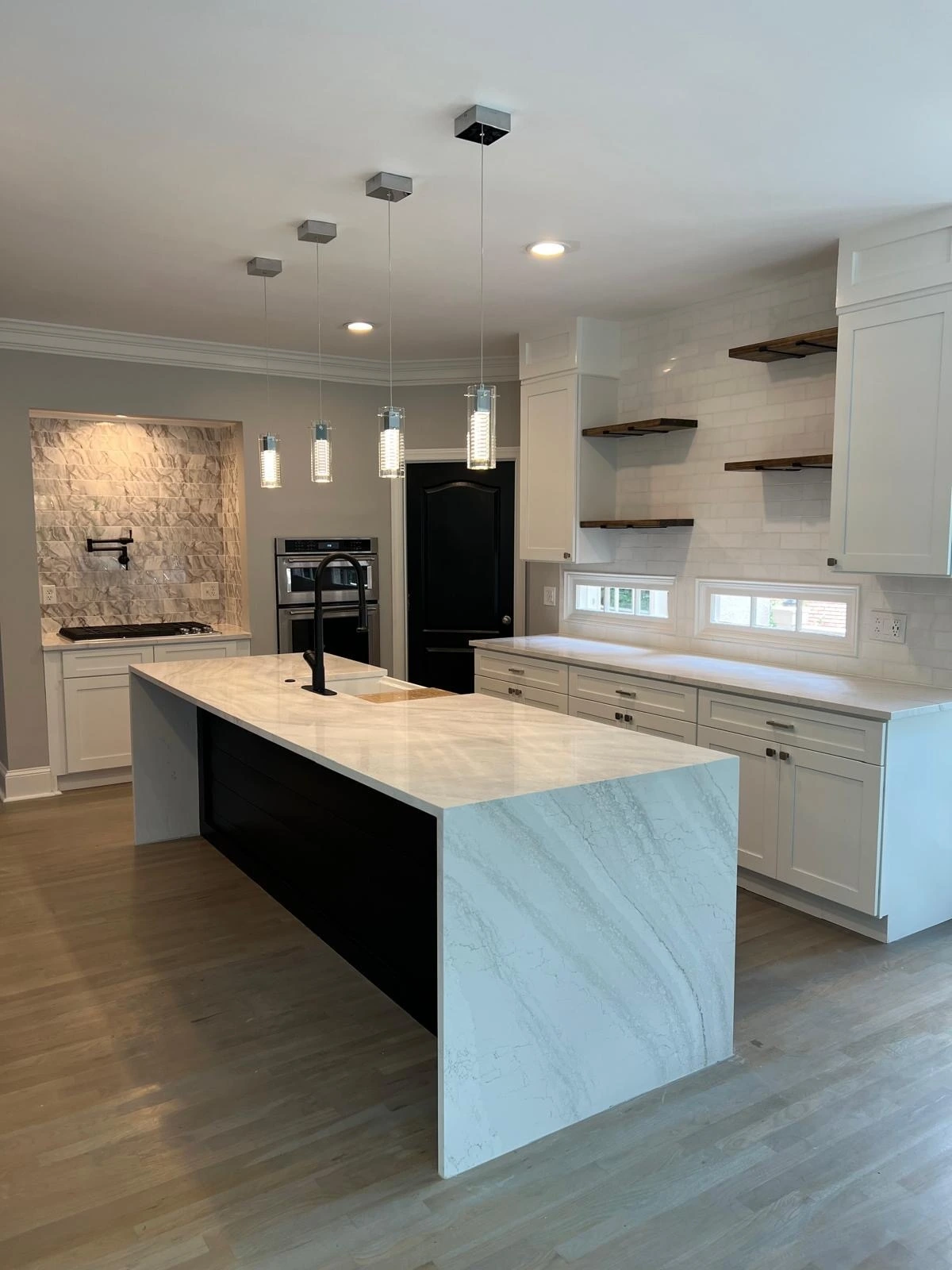 White kitchen with a stone accent wall, marble waterfall island and floating wood shelves