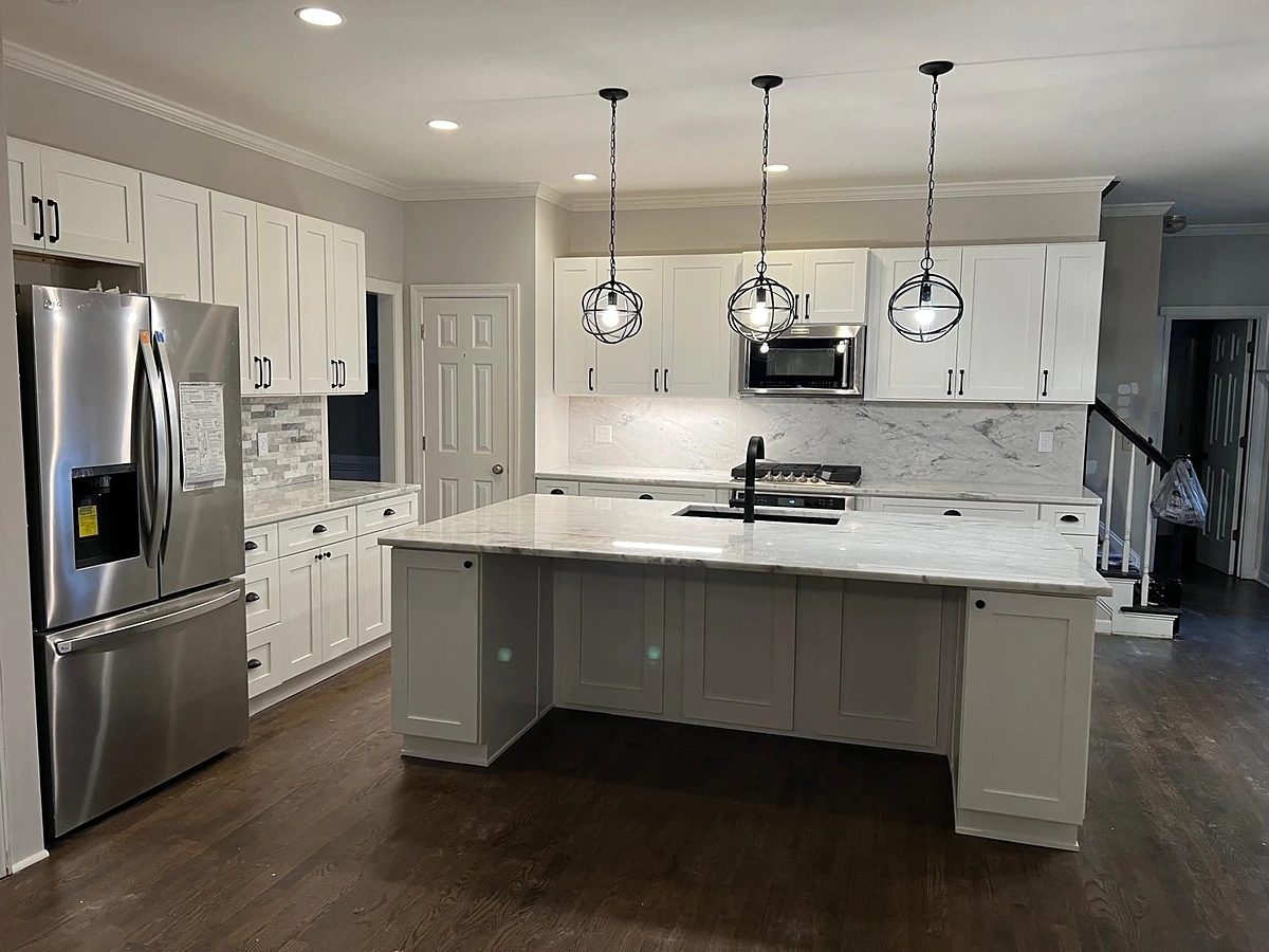 White shaker kitchen with a gray waterfall island, marble-look backsplash and pendant lighting