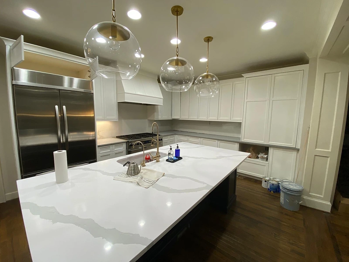 White kitchen with a wood range hood, mosaic backsplash and a large quartz island