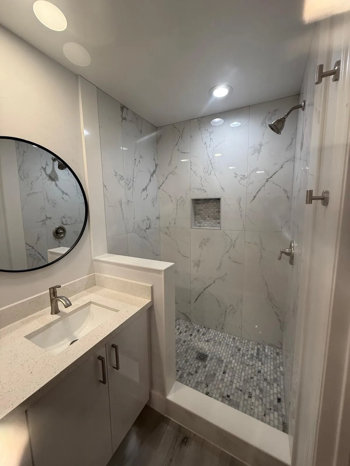 Bathroom remodel with marble shower surround, quartz vanity and round mirror — Pompano Beach, FL